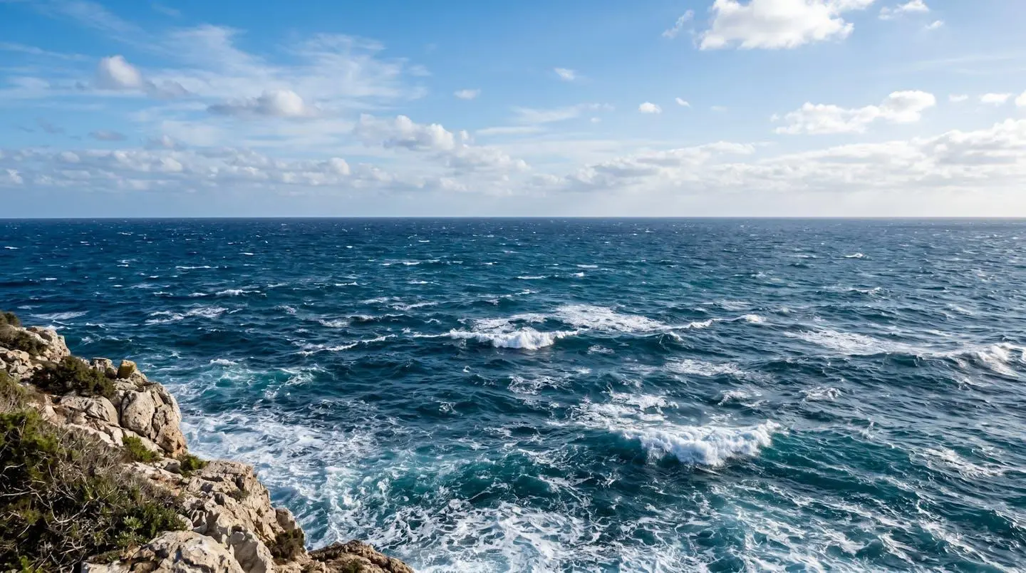 Vue large de la mer Méditerranée avec une houle modérée visible à travers des crêtes blanches espacées, un horizon bien défini et des couleurs naturelles bleu-vert profondes