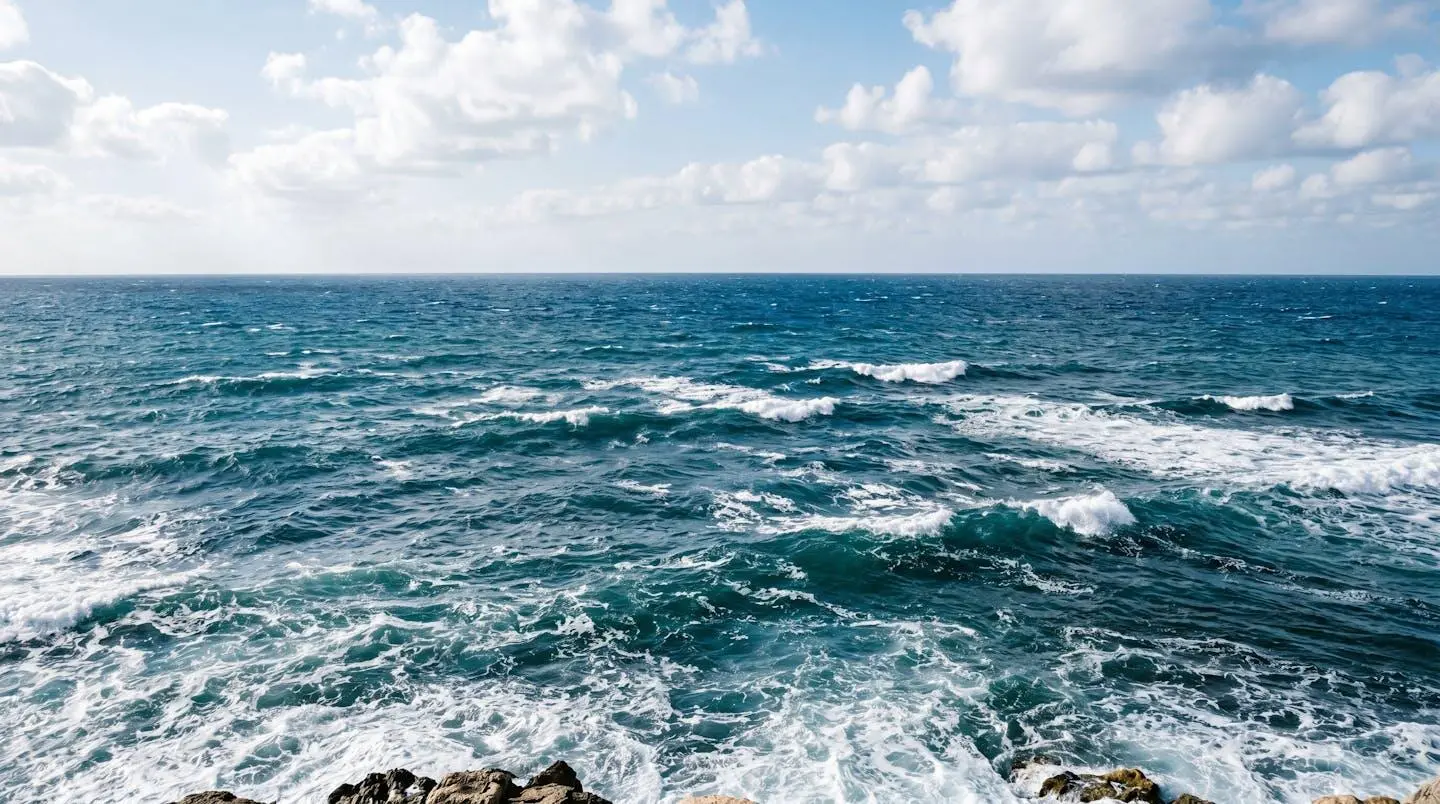 Vue large de la mer Méditerranée avec une houle modérée visible à travers des crêtes blanches espacées, un horizon bien défini et des couleurs naturelles bleu-vert profondes